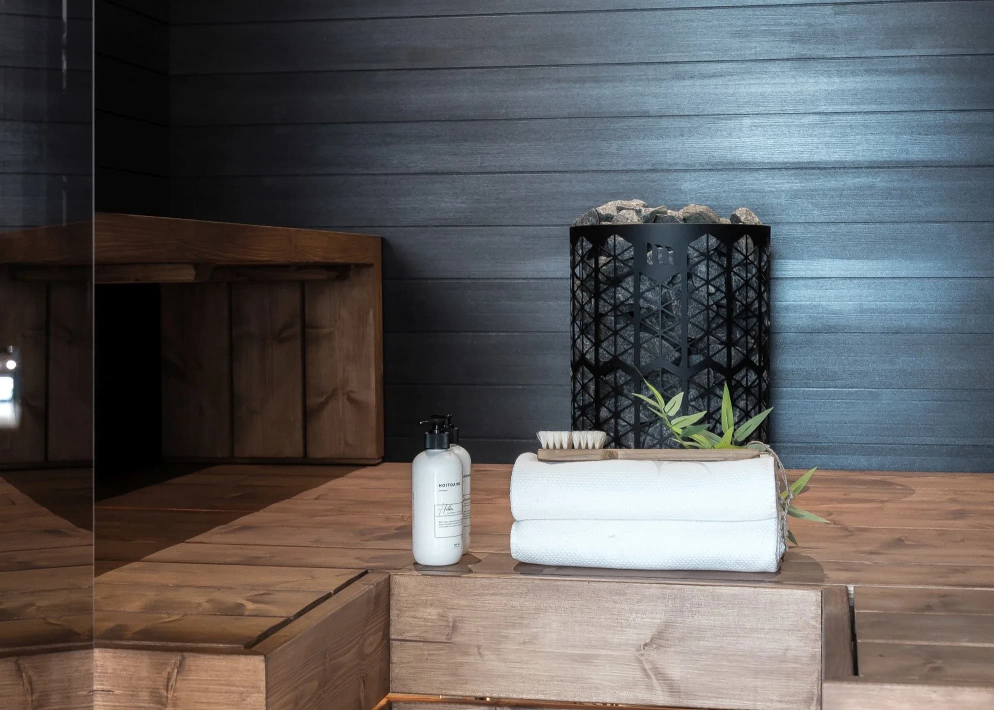 Mondex Kaira black geometric sauna heater on a dark wood bench with rolled towels